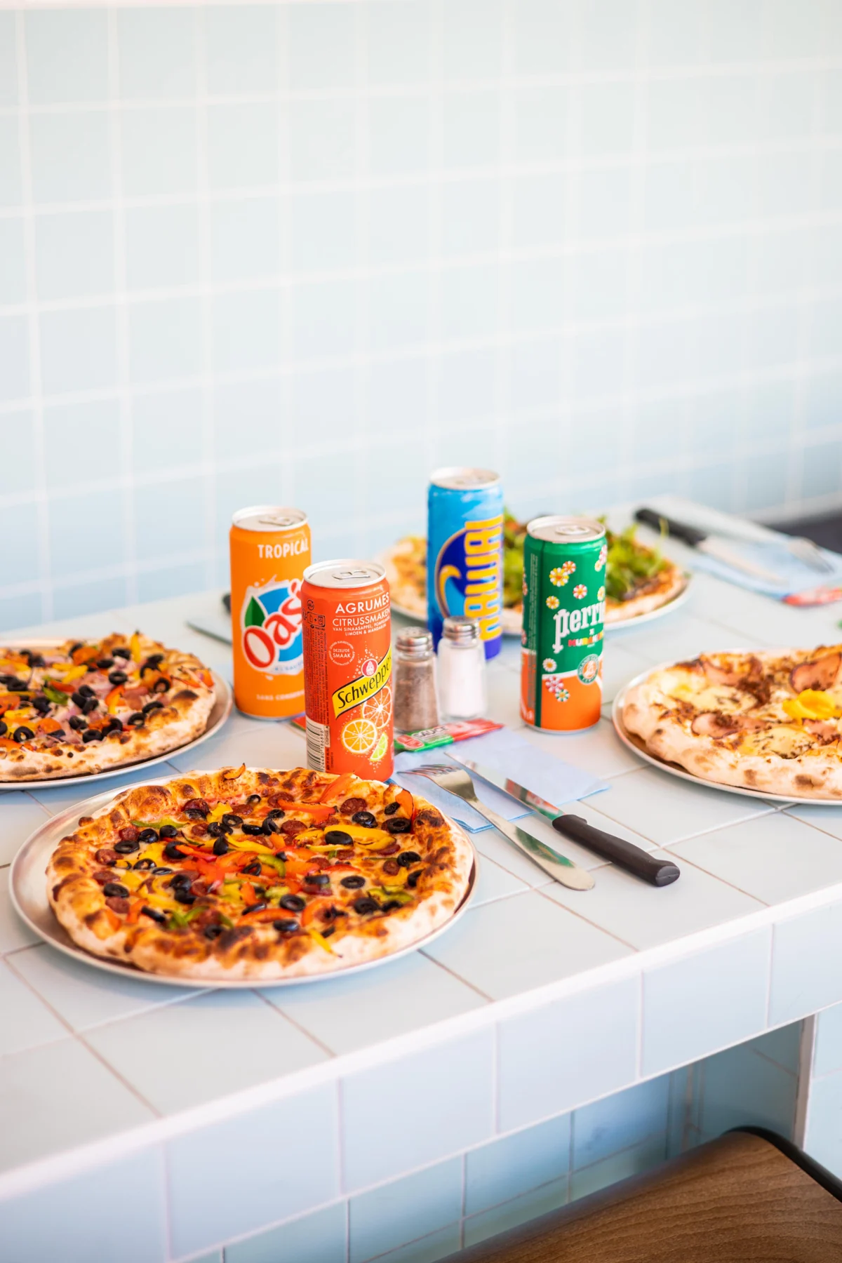 Pizzas et boissons sur une table du restaurant FRICHE, dans un décor de carrelage bleu clair